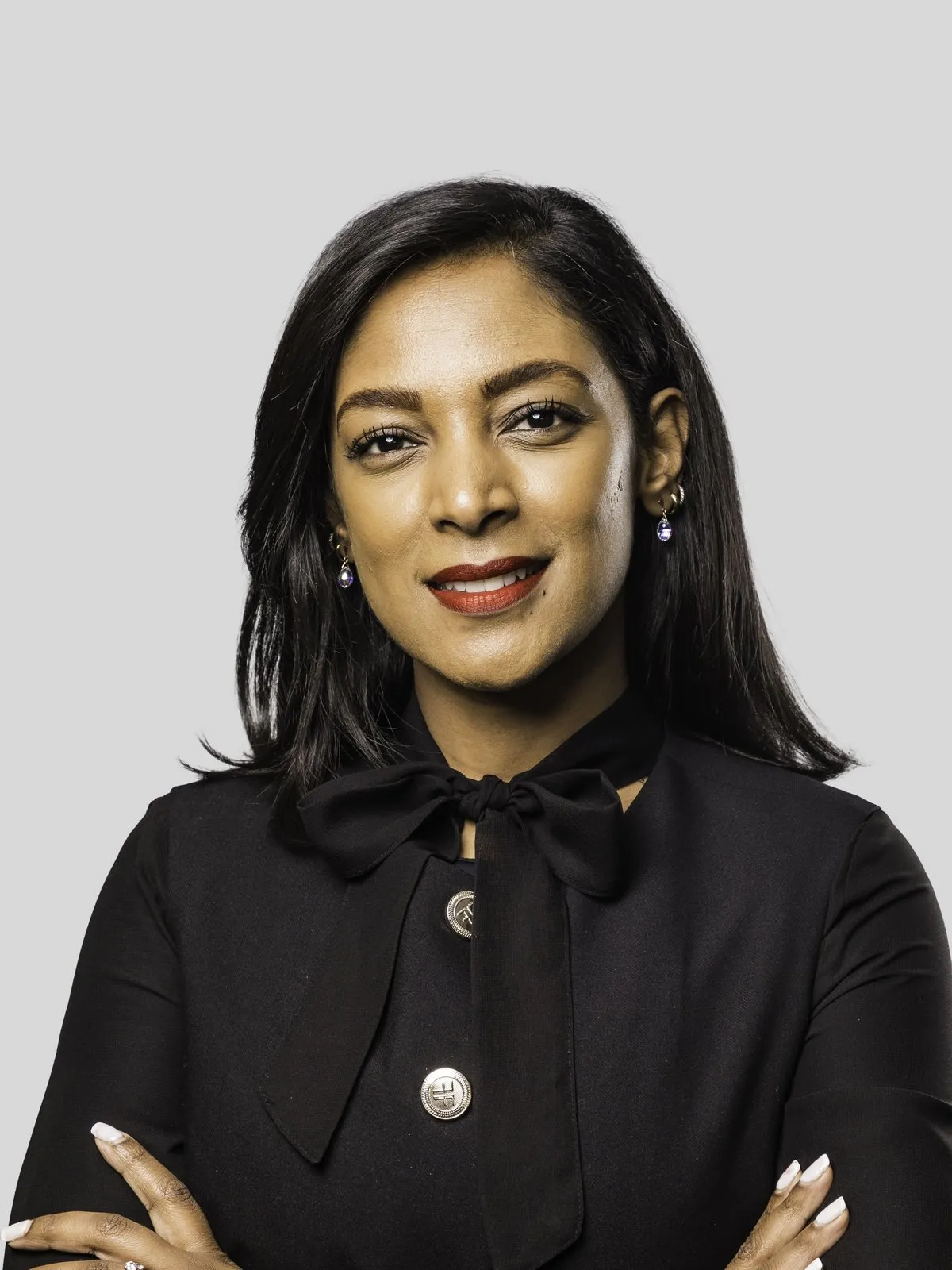 Justine Pillay, Client Coverage Consultant at TUHF Capital, smiling with arms crossed, in a black blouse with a bow, against a light grey background