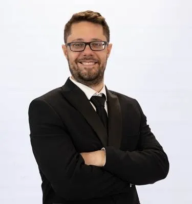 JD Paulsen, Associate at Van Deventer Dowlath & Marx Inc., in a dark suit and glasses with his arms crossed