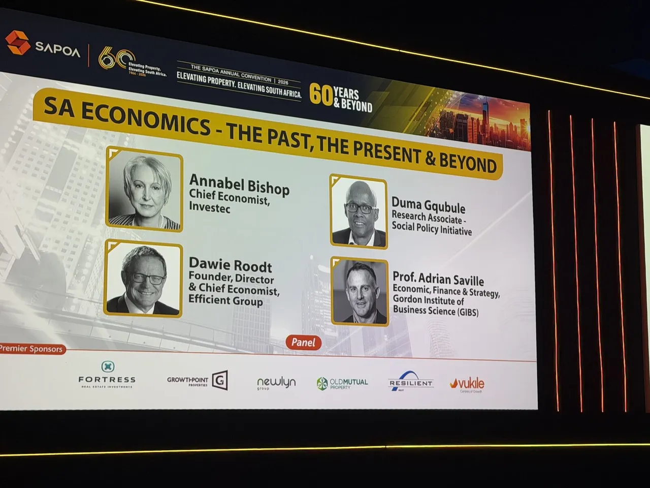 The convention screen introducing the SA Economics panel: Annabel Bishop, Chief Economist, Investec; Dawie Roodt, Founder, Director and Chief Economist, Efficient Group; Duma Gqubule, Research Associate, Social Policy Initiative; and Prof. Adrian Saville, Economics, Finance and Strategy, GIBS
