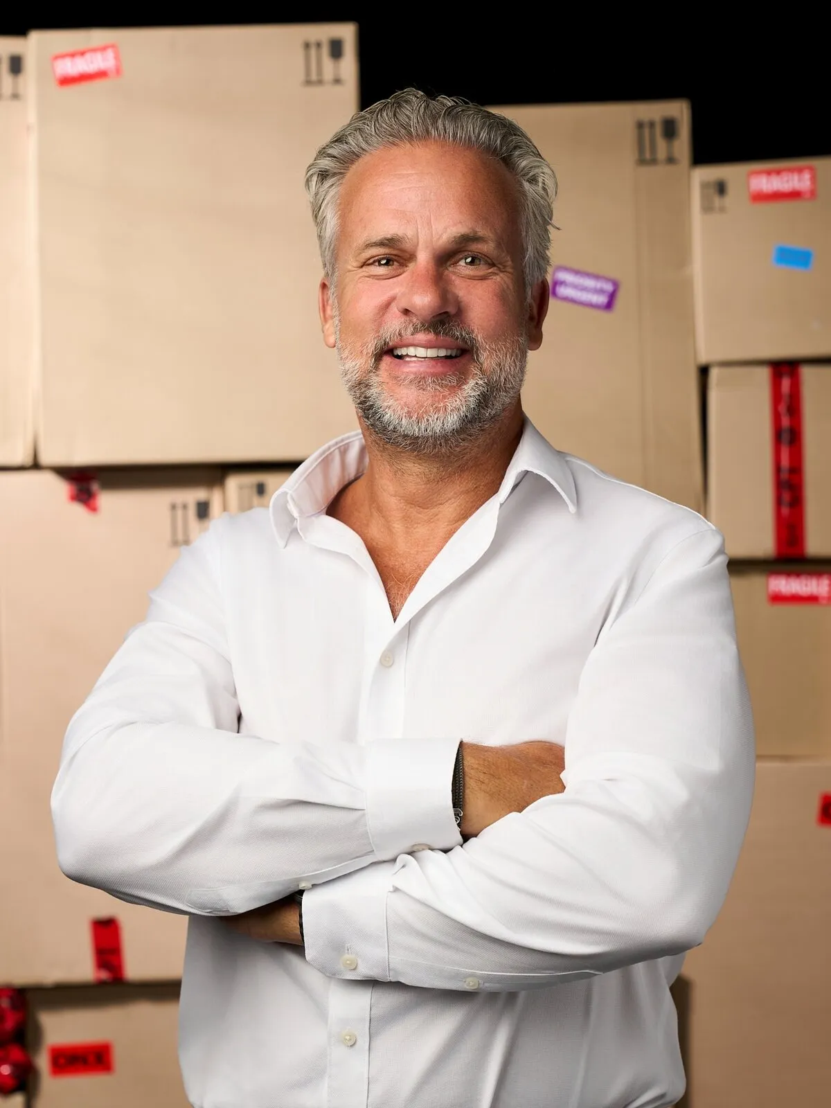 Andrew Van Der Velde, CEO of DPD South Africa, smiling with arms folded in a white shirt, in front of stacked parcels