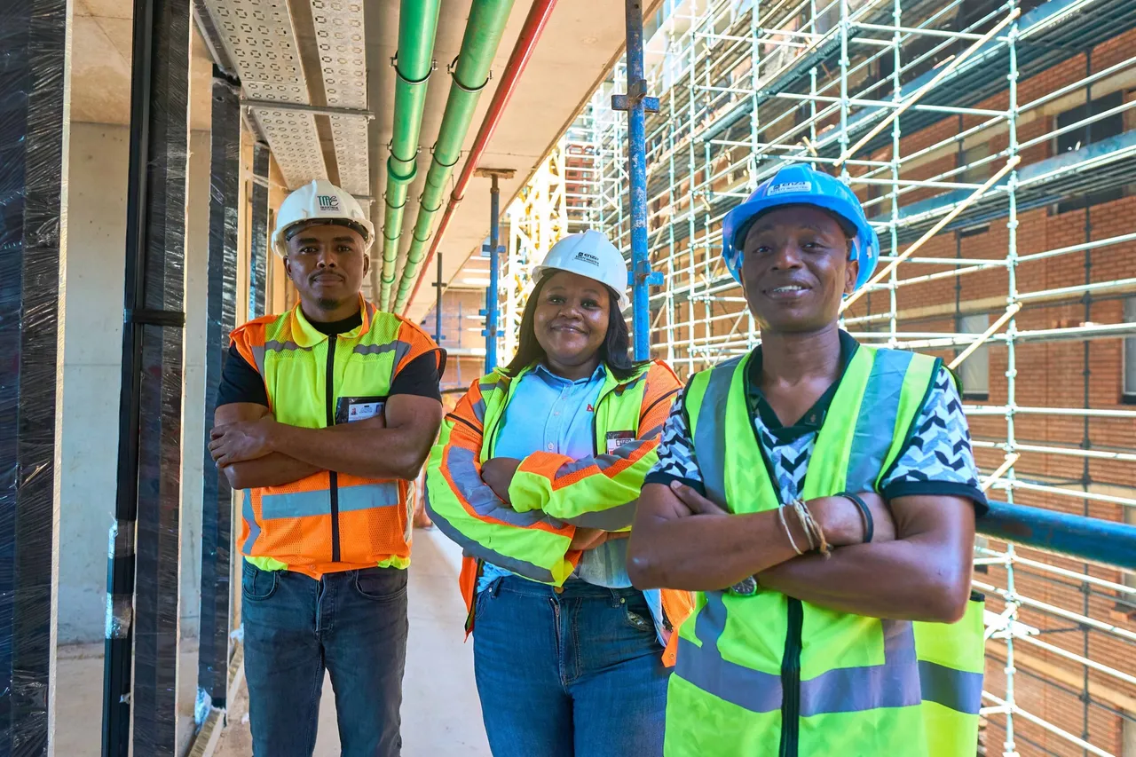 Three members of the construction team in hard hats and hi-vis vests with arms crossed on the Thrive Student Living site in Berea, Durban, with scaffolding and brickwork behind