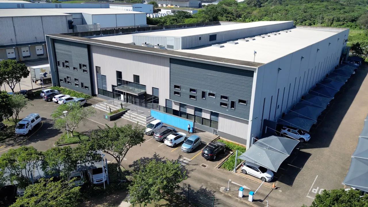 Aerial view of a large white-roofed industrial building with grey cladding, a glass entrance and a car park, surrounded by trees at Riverhorse Valley in Durban