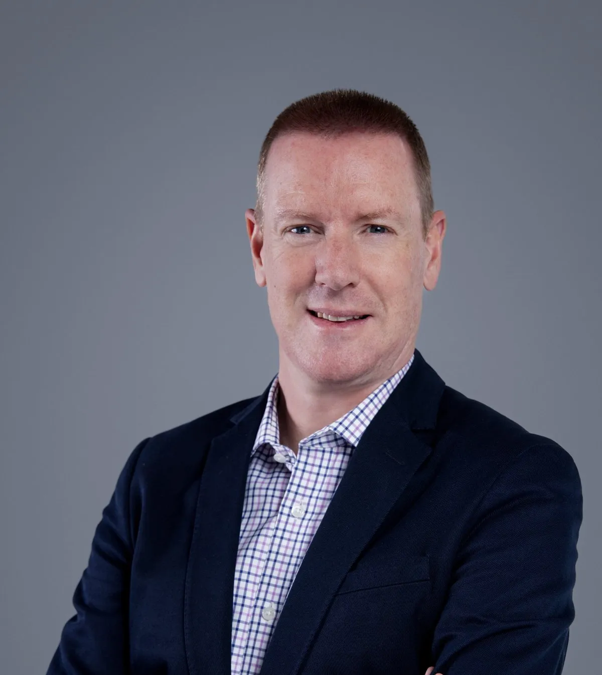 Andrew Robinson, Sector Head of Real Estate at Standard Bank Corporate and Investment Banking, smiling, in a navy blazer and checked shirt against a grey background