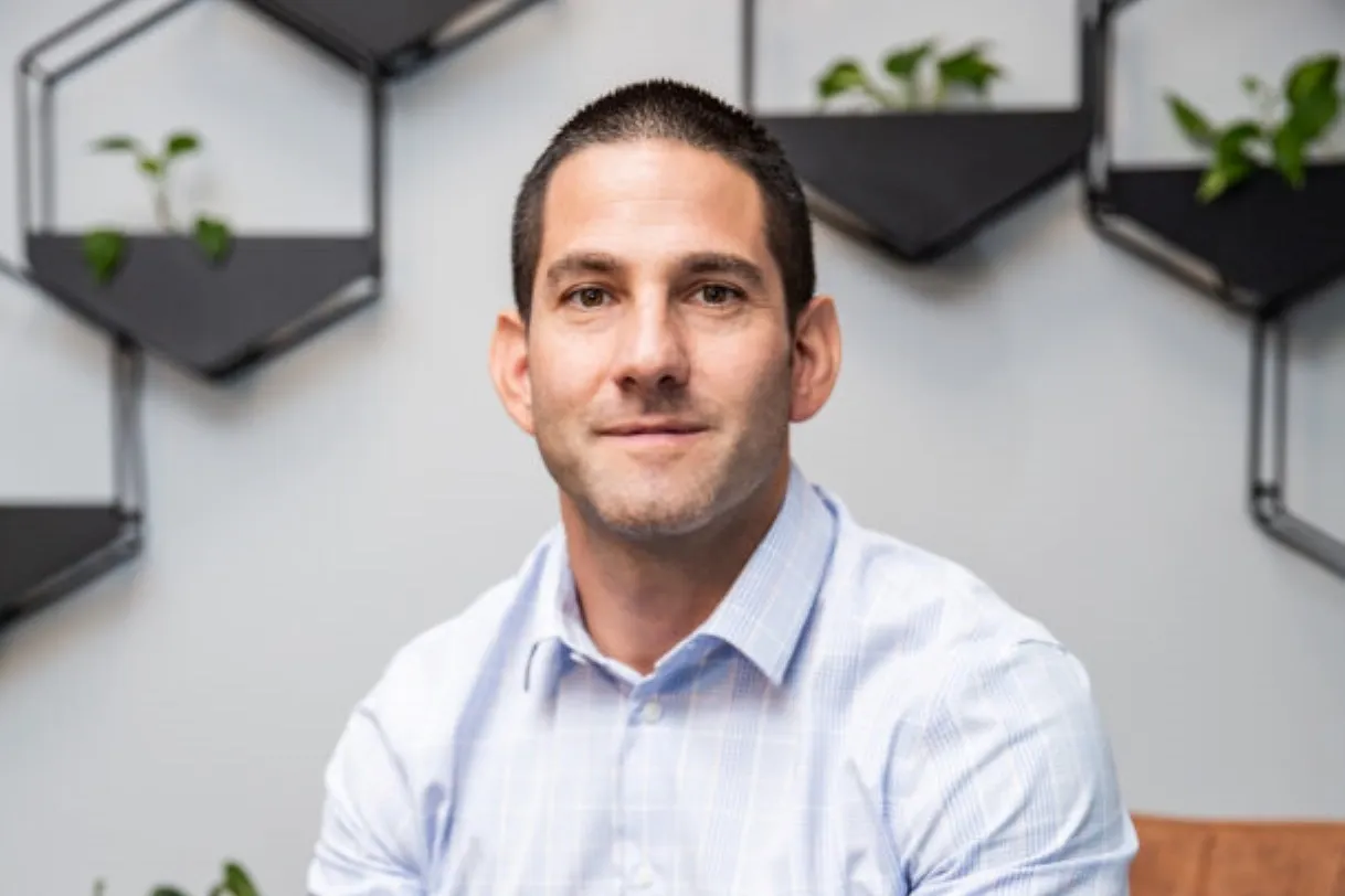 Grant Silverman, director of Abland Property Developers, in a light blue checked shirt, seated in front of a grey wall with hexagonal plant shelves