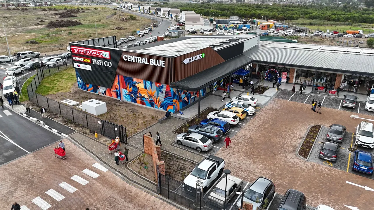 Aerial view of Central Blue Shopping Centre: the Central Blue sign over a colourful mural, Superspar, Fish Co and Clicks signage, a covered walkway and shoppers crossing the car park