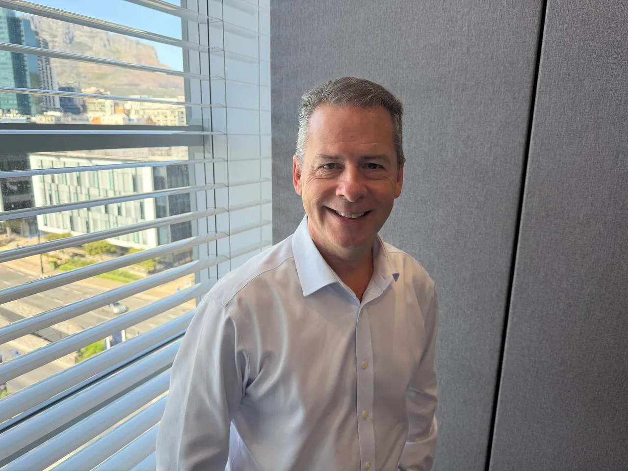 Hammerson chief executive Rob Wilkinson smiling in a light blue shirt beside a window overlooking Cape Town