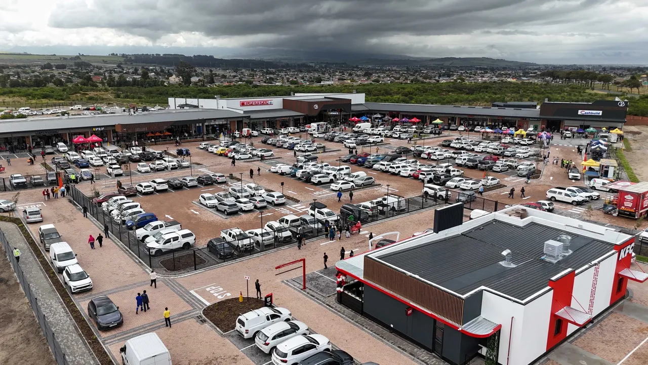 Aerial view of Central Blue Shopping Centre in Blue Downs, Cape Town: a long single-storey row of shops behind a full car park, with a KFC drive-through in the foreground and housing stretching to the hills under a grey sky