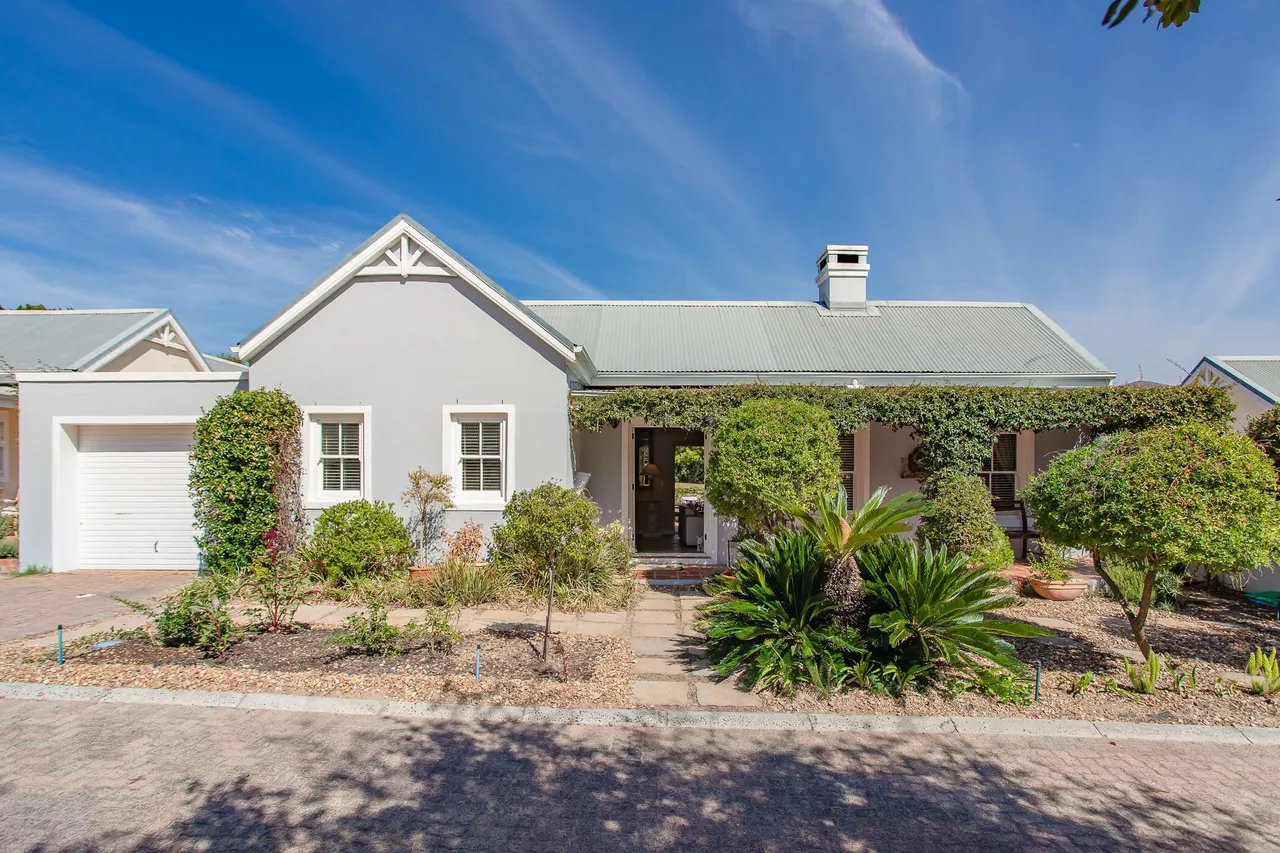 A single-storey Cape cottage-style home with a grey-green corrugated roof, a vine-covered stoep and a cycad garden in a Franschhoek estate