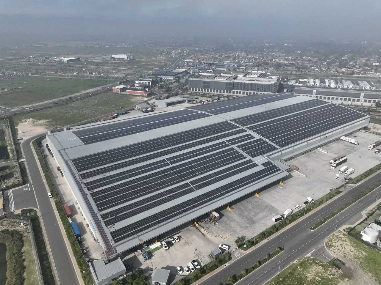 Aerial view of the Massmart Distribution Centre in Brackengate, Cape Town, its large warehouse roof covered in rows of solar panels, with loading bays and roads around it
