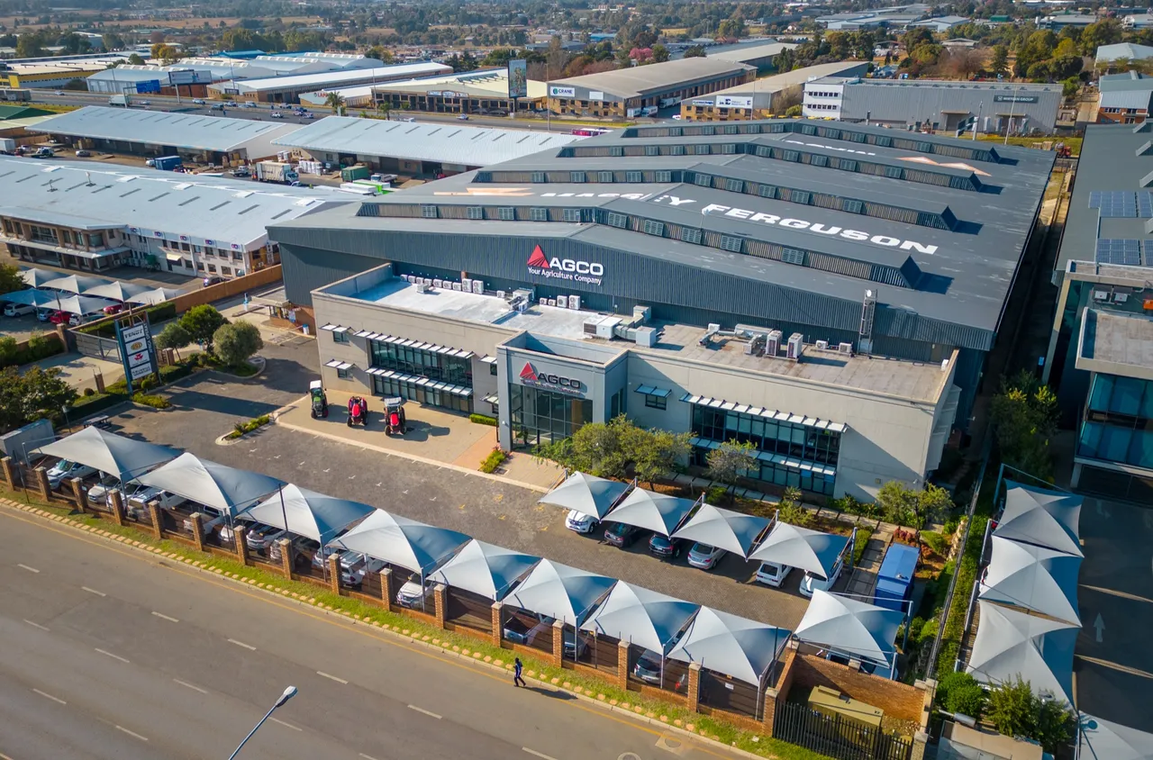 Aerial view of 16 Pomona, a large industrial building with AGCO signage and Massey Ferguson lettering on its roof, with shaded parking along the street